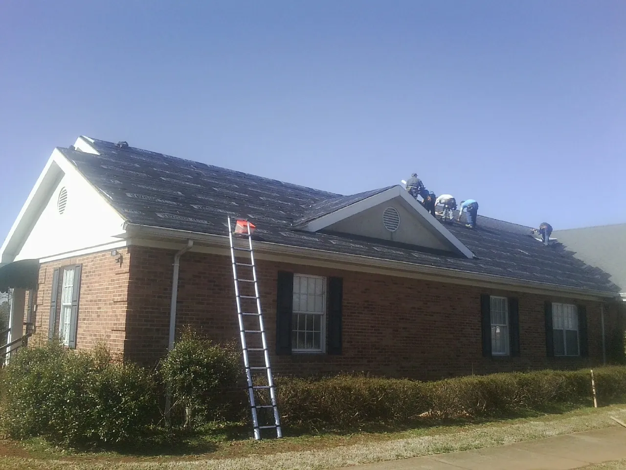 Crew tearing shingles off a brick ranch roof with a ladder set — Metal Roof Repair work by our crew in Keosauqua