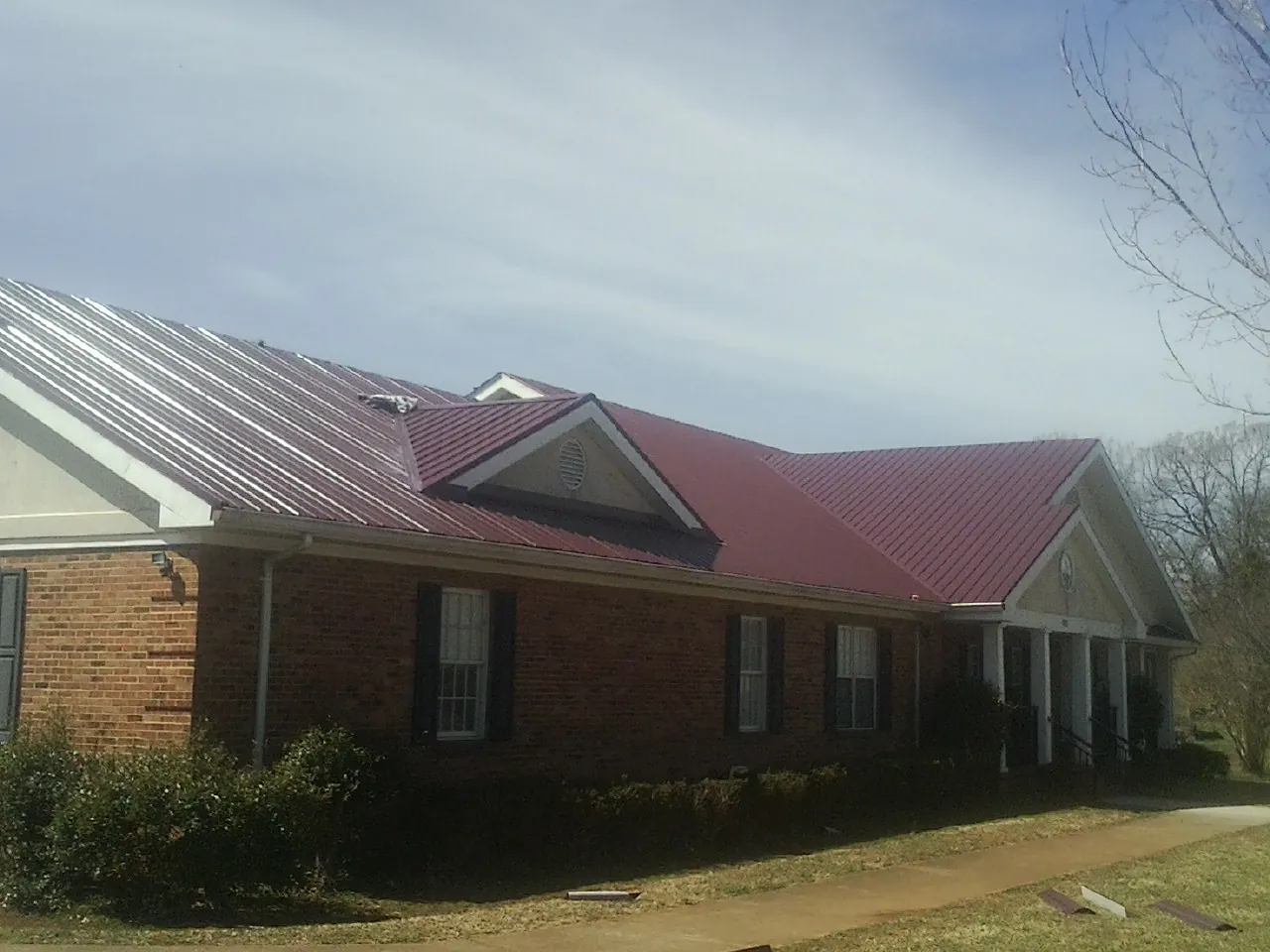 Red metal roof with gabled entries on a long brick building, from a Hail Damage Roof Repair job in Keosauqua
