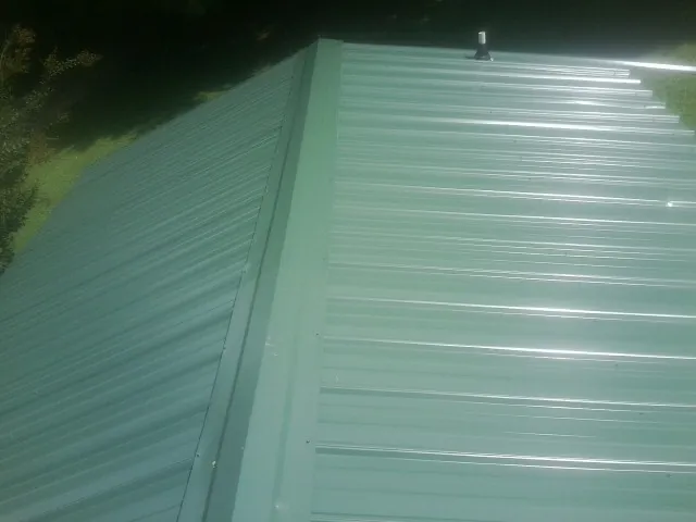 New green metal panels meeting at the ridge of a roof — Flat Roof Repair work by our crew in Keosauqua