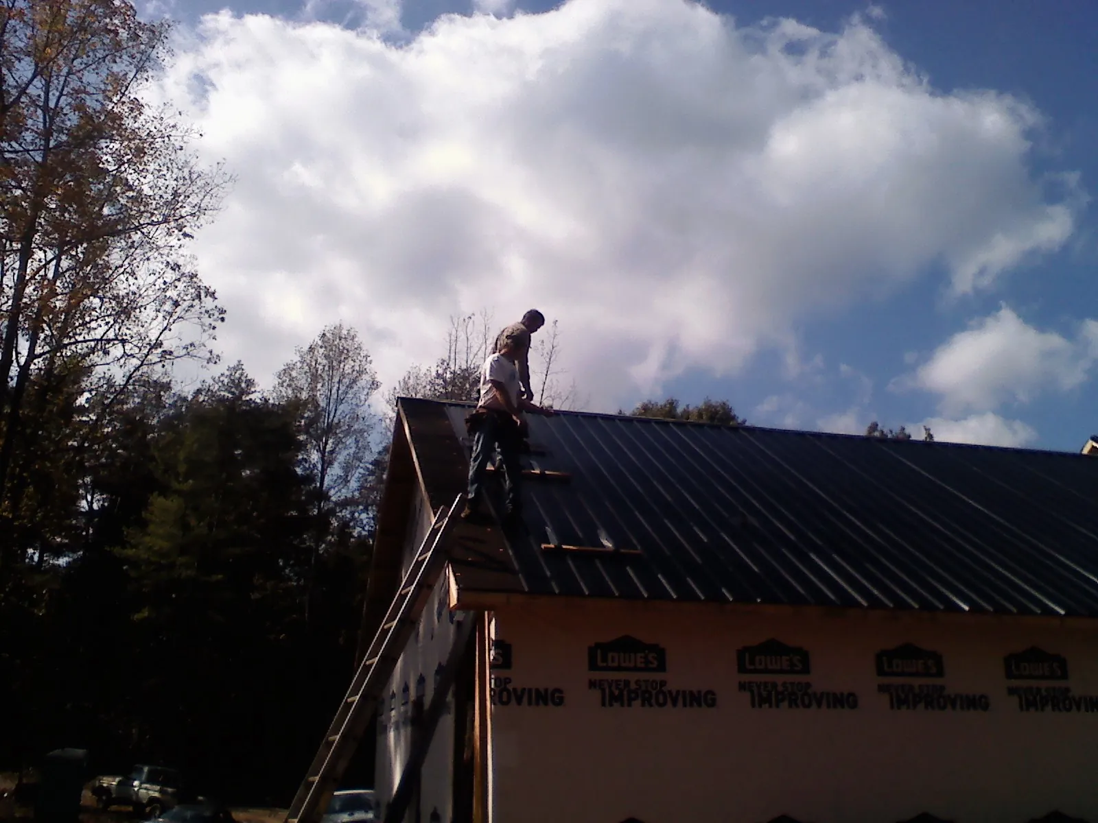 Roofer fastening dark metal panels high against a cloudy sky, from a Roof Inspection job in Keosauqua
