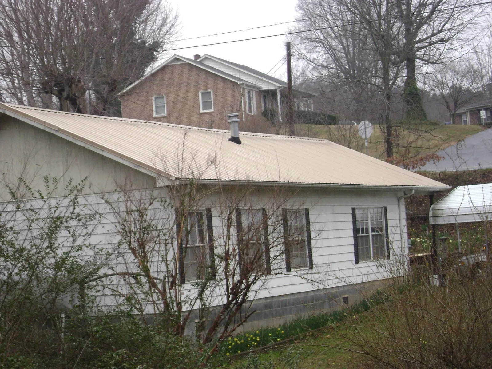 Tan metal roof on a white sided house set into a hillside — Commercial Roofing by Roofing Brothers in Keosauqua